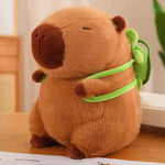 Capybara plush with a brown body and a green backpack, sitting on a wooden surface.