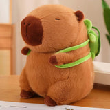 Capybara plush with a brown body and a green backpack, sitting on a wooden surface.