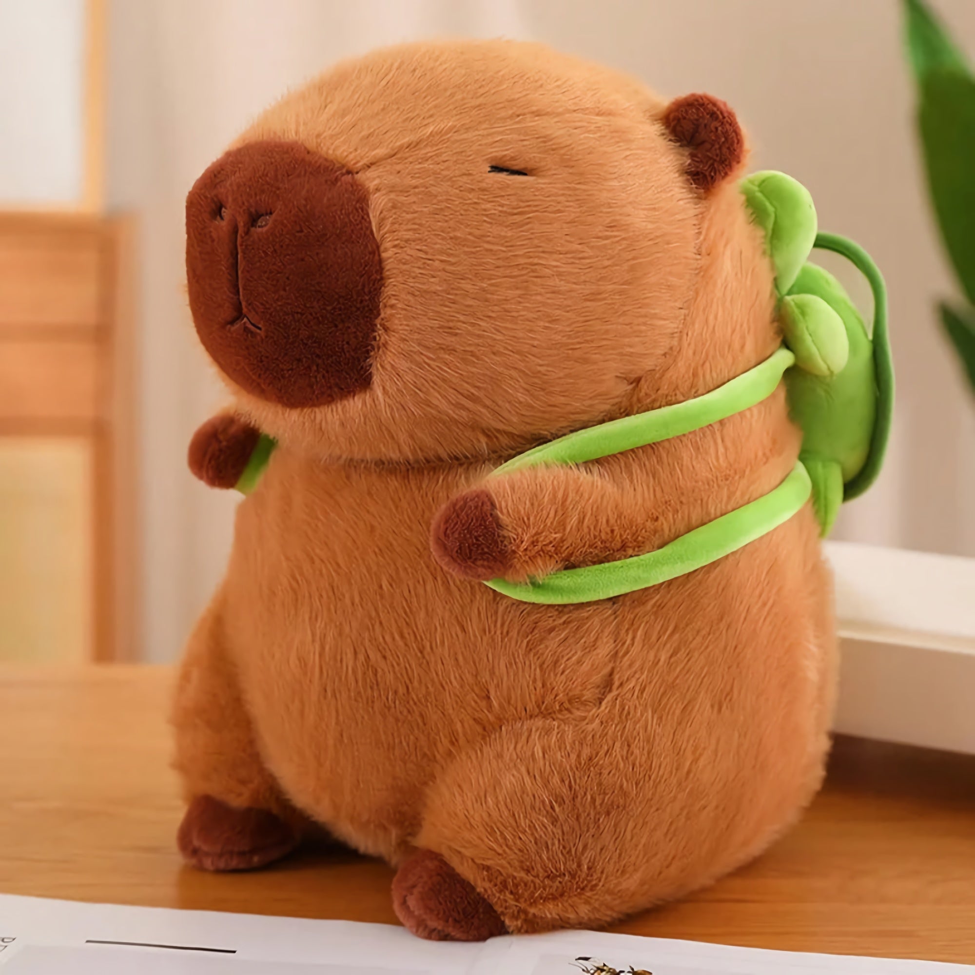 Capybara plush with a brown body and a green backpack, sitting on a wooden surface.