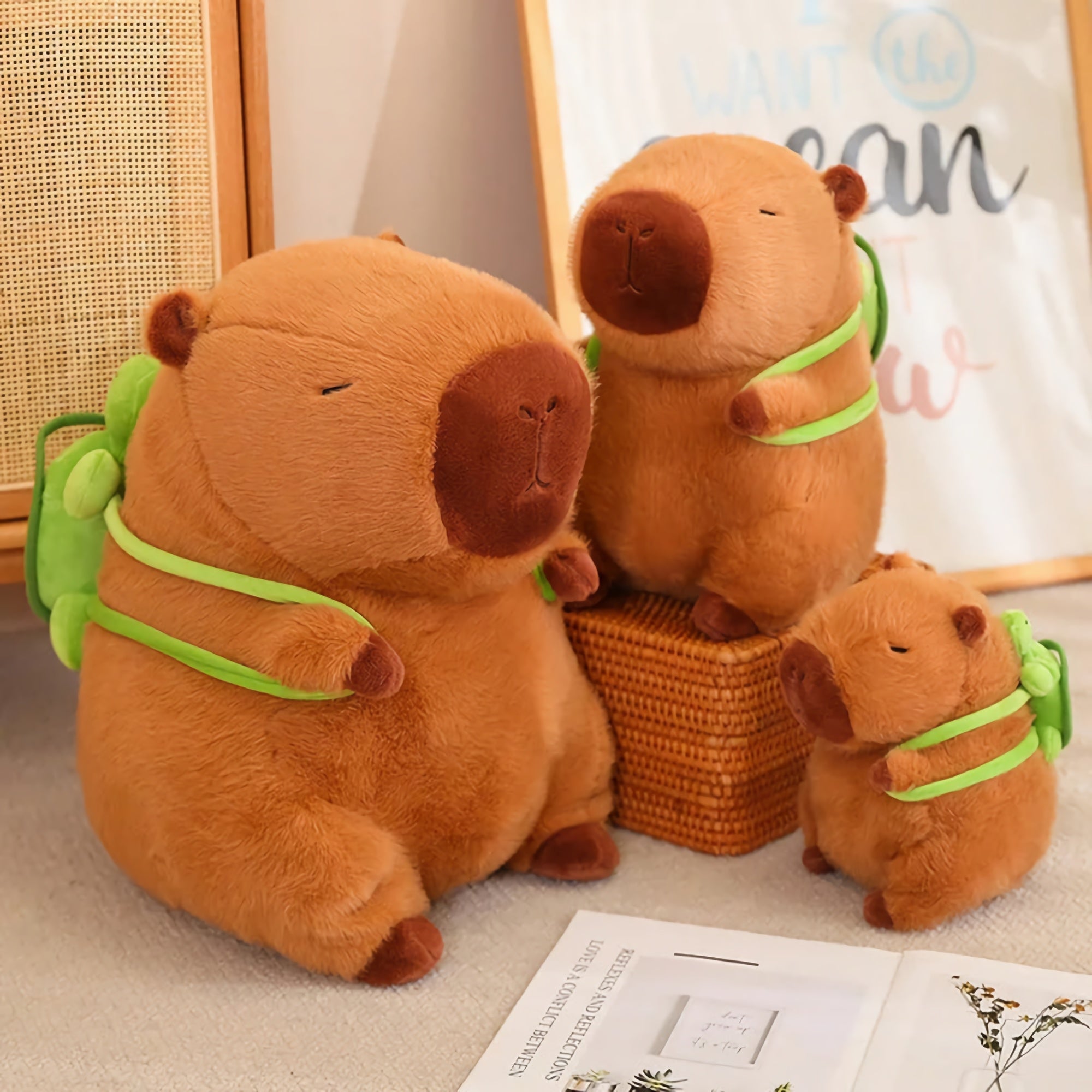Three capybara plush with green backpacks, sitting on a surface with a decorative background.