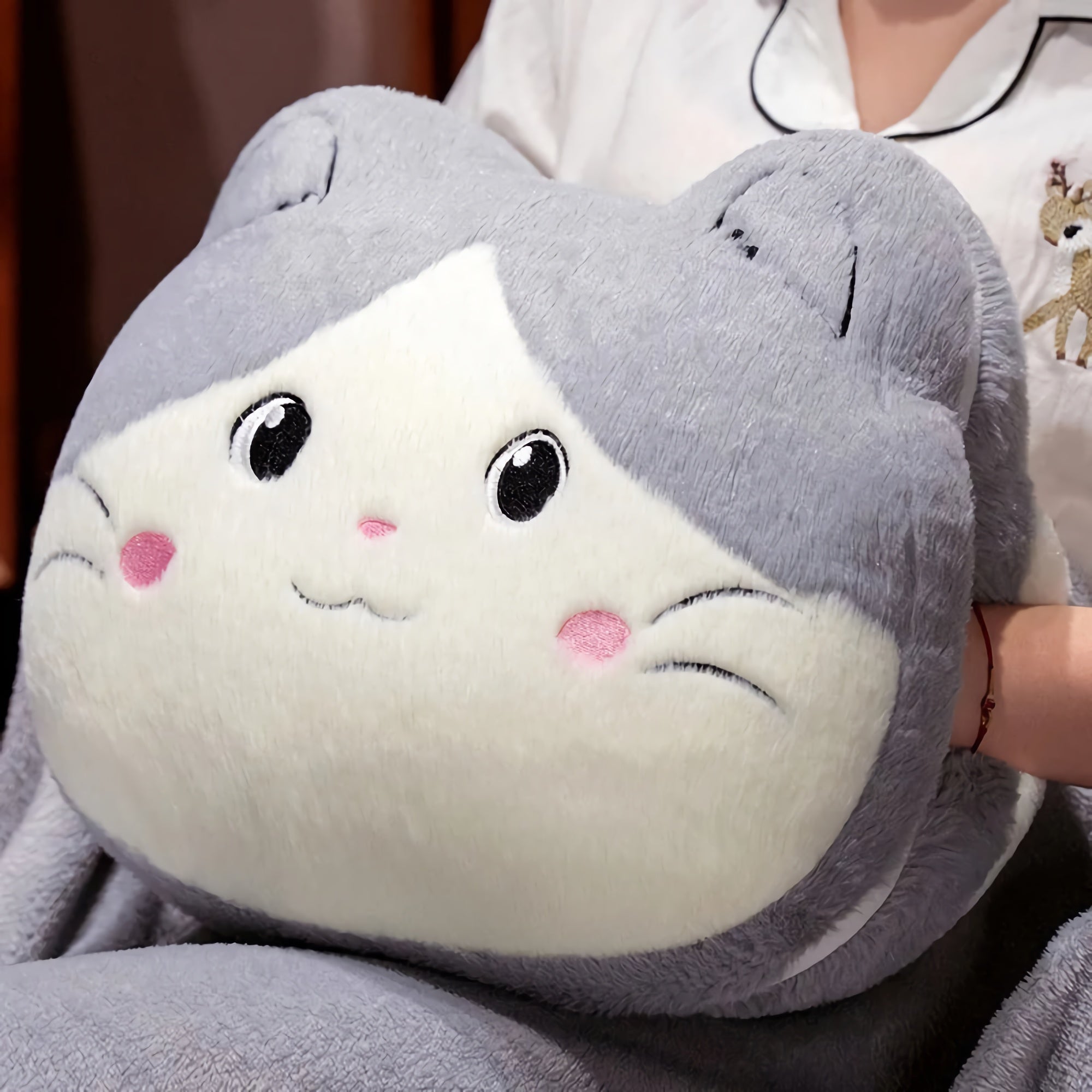 Plush cat-shaped pillow with gray and white fur, held by a person in pajamas.