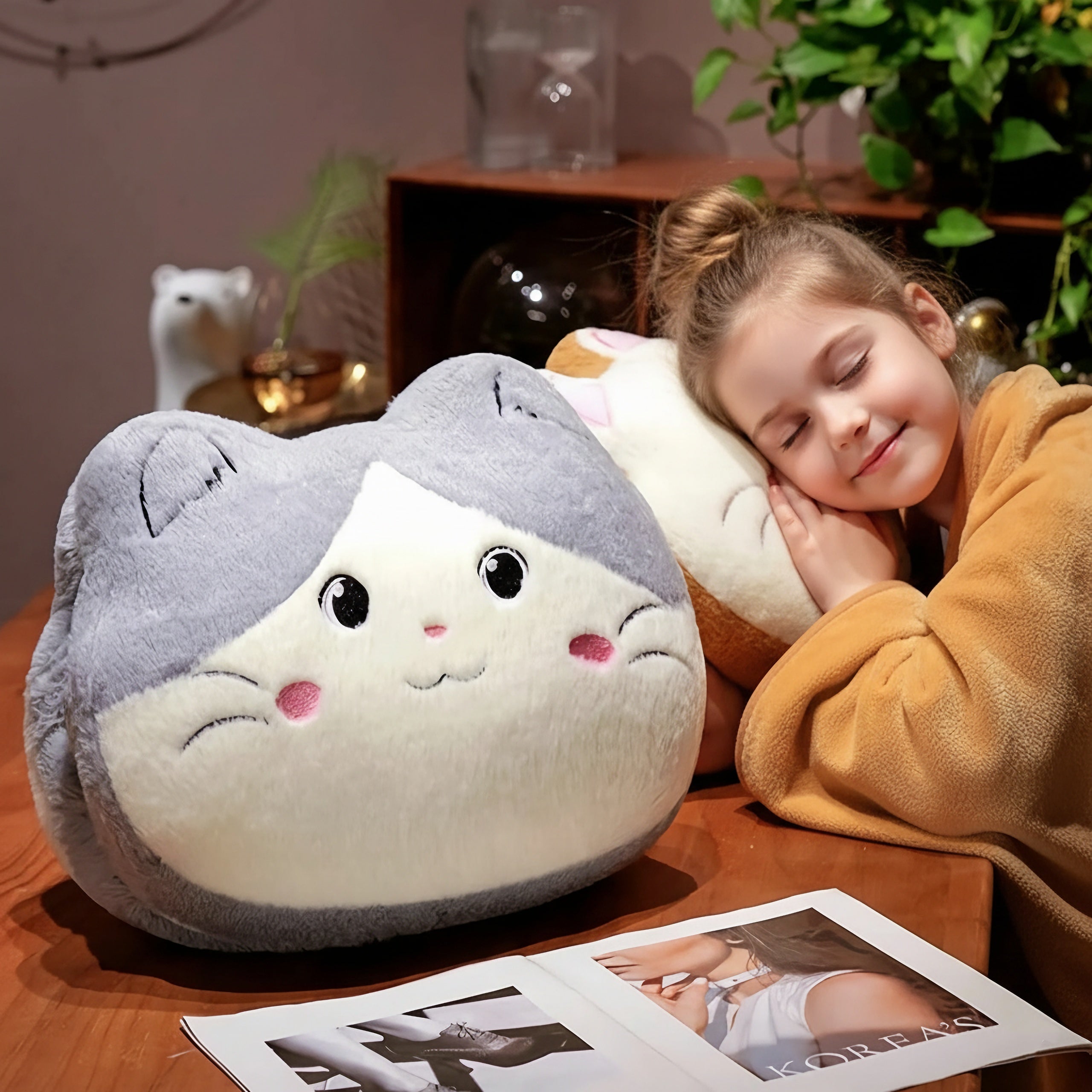 Child resting on a plush cat-shaped pillow at a table with a magazine.