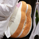 A plush, sandwich-shaped pillow rests against a person's side while they sit in a chair.