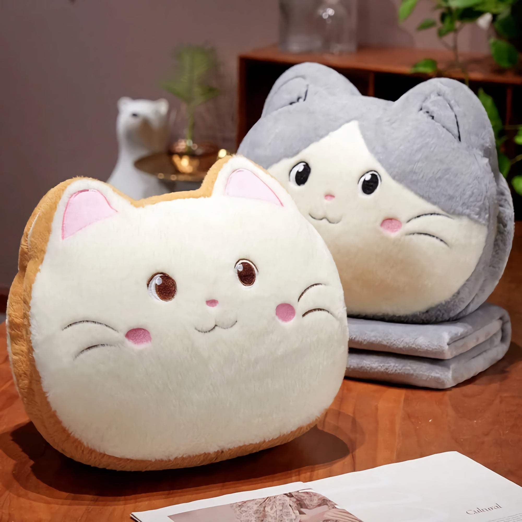 Two plush cat-shaped pillows with smiling faces on a wooden table.