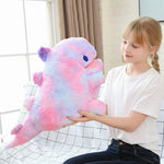 A girl holds a large, colorful dinosaur plush toy while sitting on a couch.