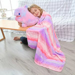 A child sits on the floor, hugging a plush dinosaur pillow while wrapped in a colorful striped blanket.