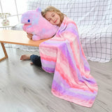 A child sits on the floor, hugging a plush dinosaur pillow while wrapped in a colorful striped blanket.