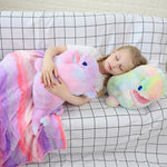 Child sleeping on a couch with a colorful blanket, hugging two plush dinosaur pillows.