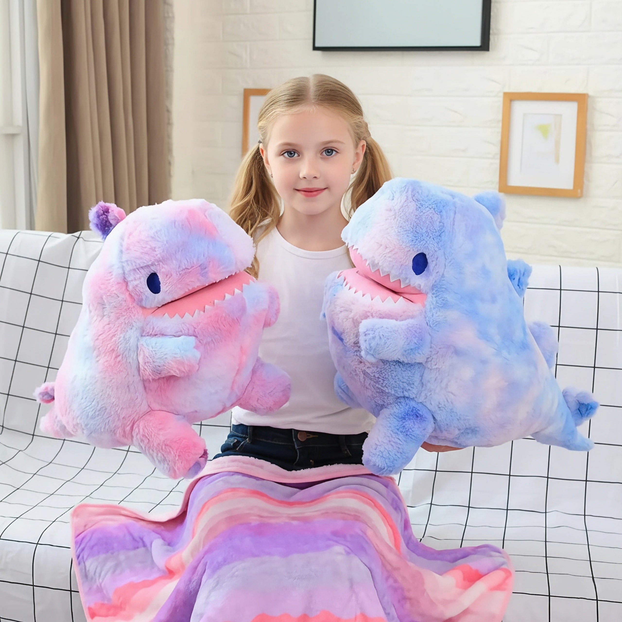 Girl holding two plush dinosaur toys with a colorful blanket on her lap.