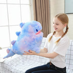 A girl holds a large, colorful plush dinosaur pillow while sitting on a couch with a grid-patterned blanket.