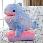 Blue and pink plush dinosaur toy sitting on a matching folded blanket.