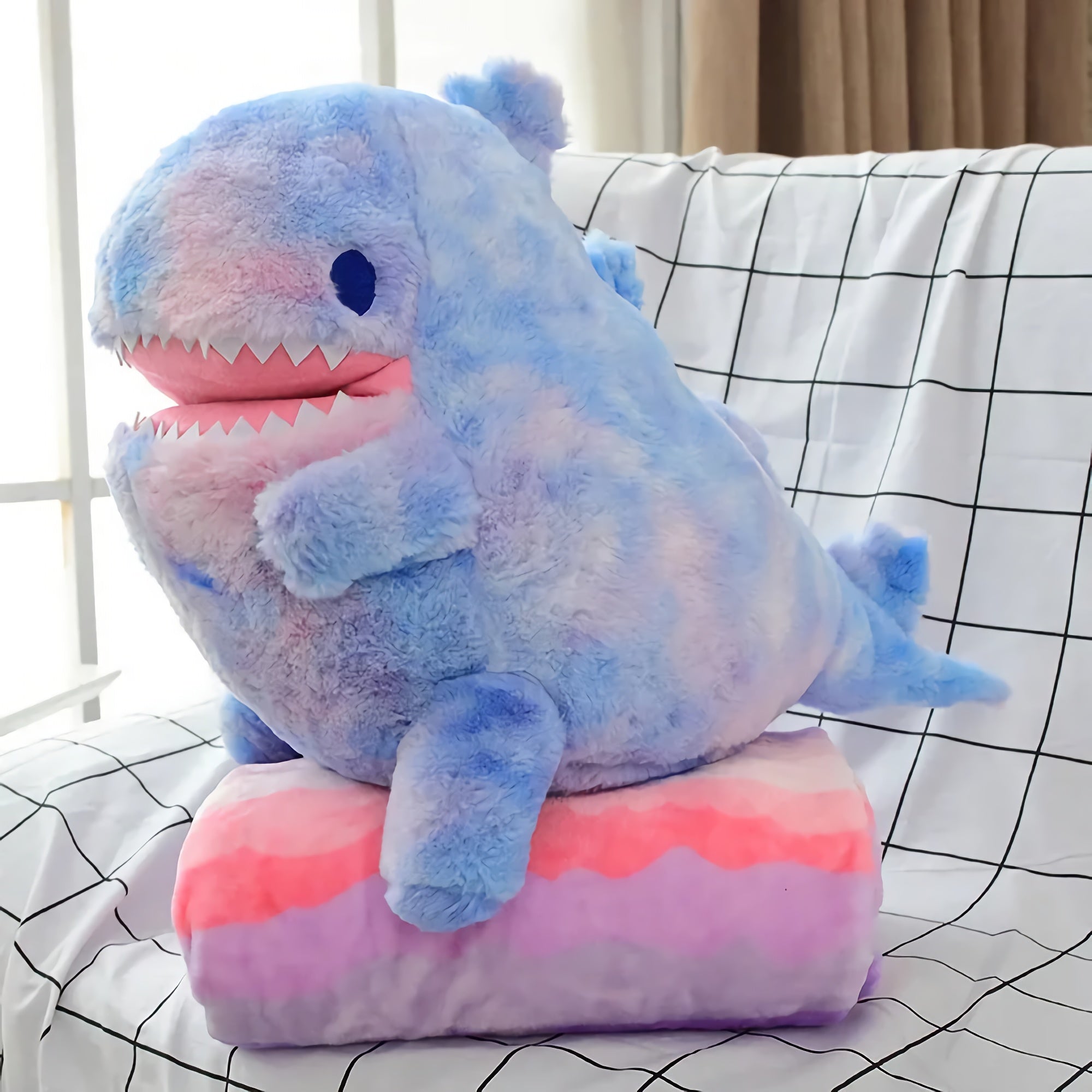 Blue and pink plush dinosaur toy sitting on a matching folded blanket.