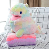 A colorful dinosaur plush pillow sits on a matching blanket, both displayed on a grid-patterned surface.