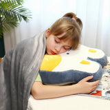 Child sleeping with a gray blanket, hugging a plush pillow shaped like an animal, in a cozy indoor setting.