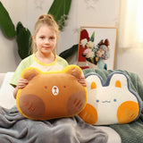 A girl holds a bear-shaped pillow while sitting on a couch with a rabbit-shaped pillow beside her, wrapped in a blanket.