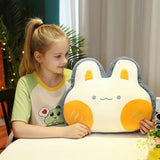 A child sits at a table holding a plush pillow shaped like a bunny with orange accents.