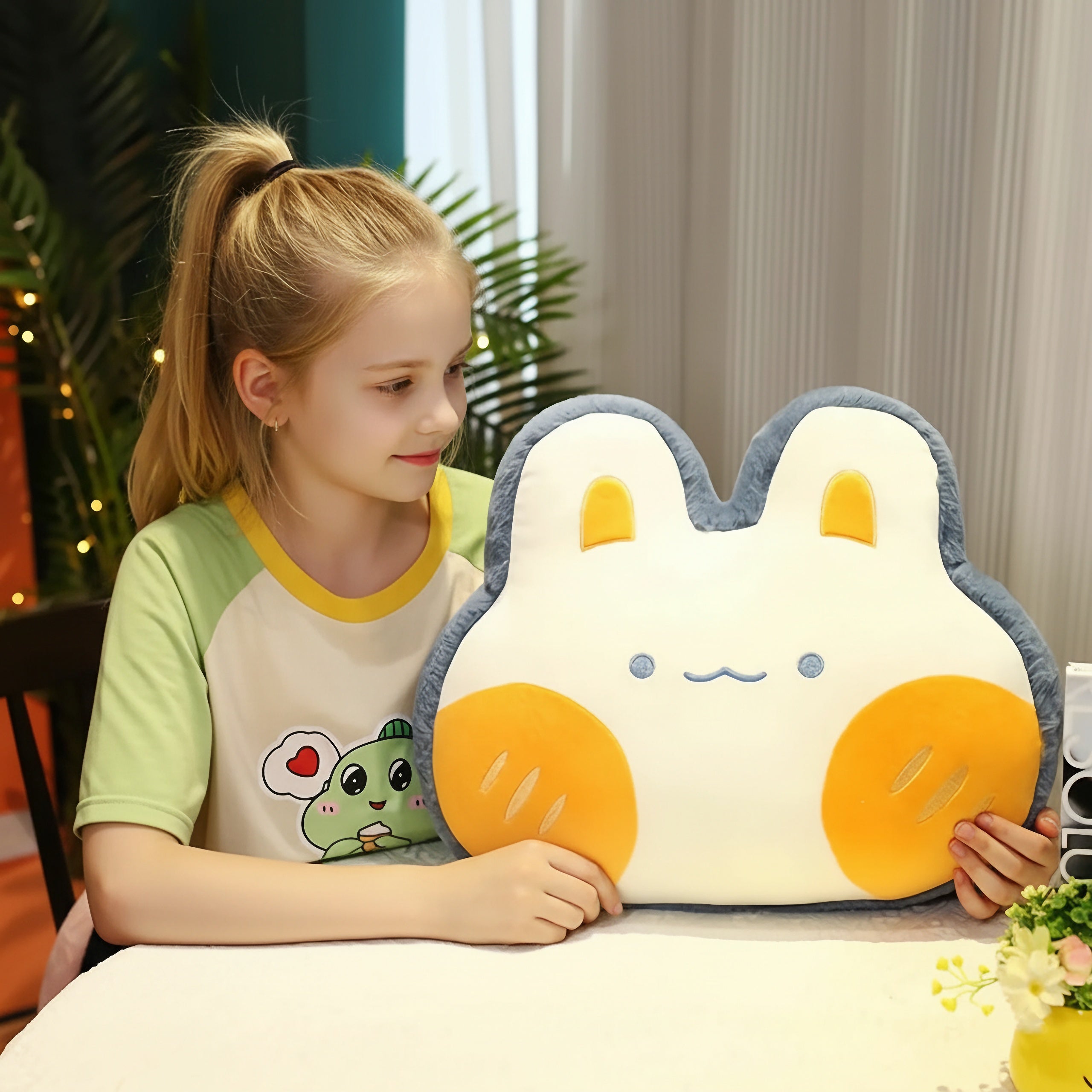 A child sits at a table holding a plush pillow shaped like a bunny with orange accents.