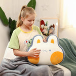 Girl sitting on a couch, holding a plush pillow shaped like a rabbit, with a gray blanket draped over her legs.