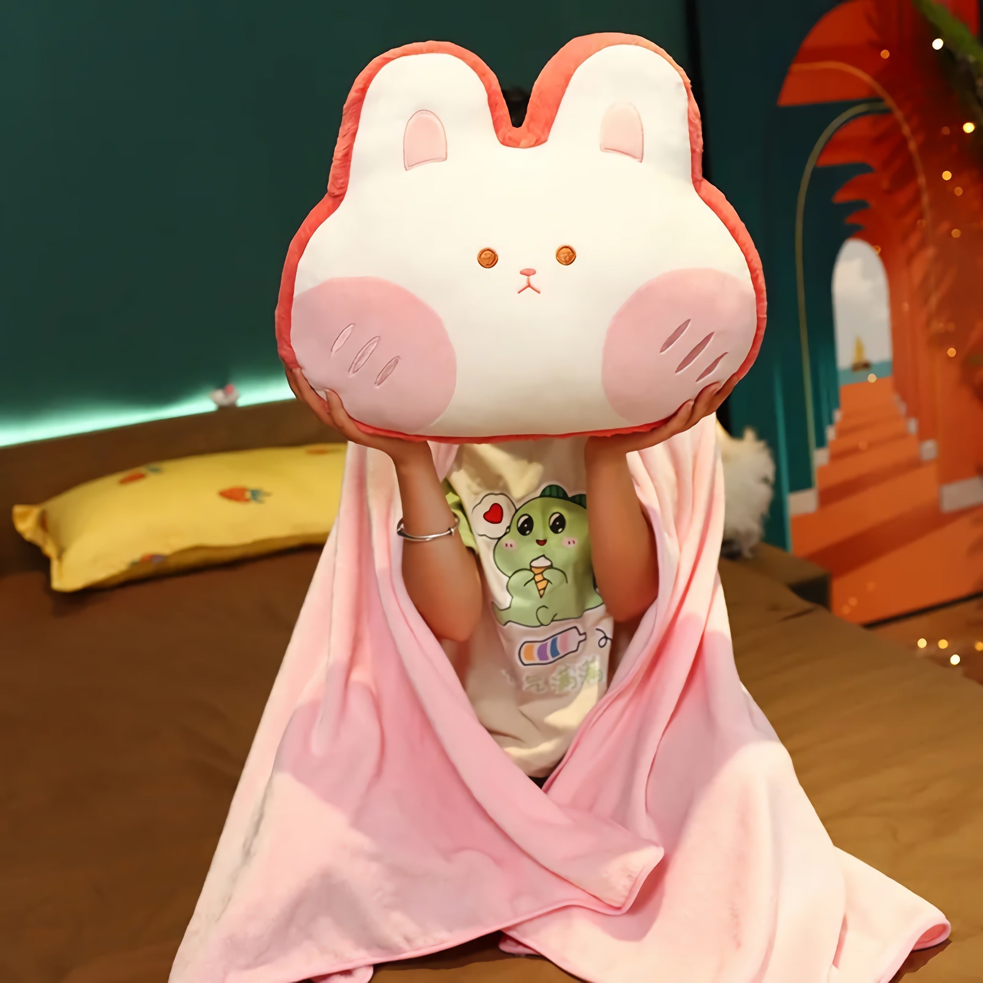 Child sitting on a bed, holding a plush bunny pillow while wrapped in a pink blanket.