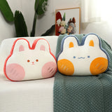 Two plush pillows shaped like bunnies with pink and orange accents on a textured blanket.