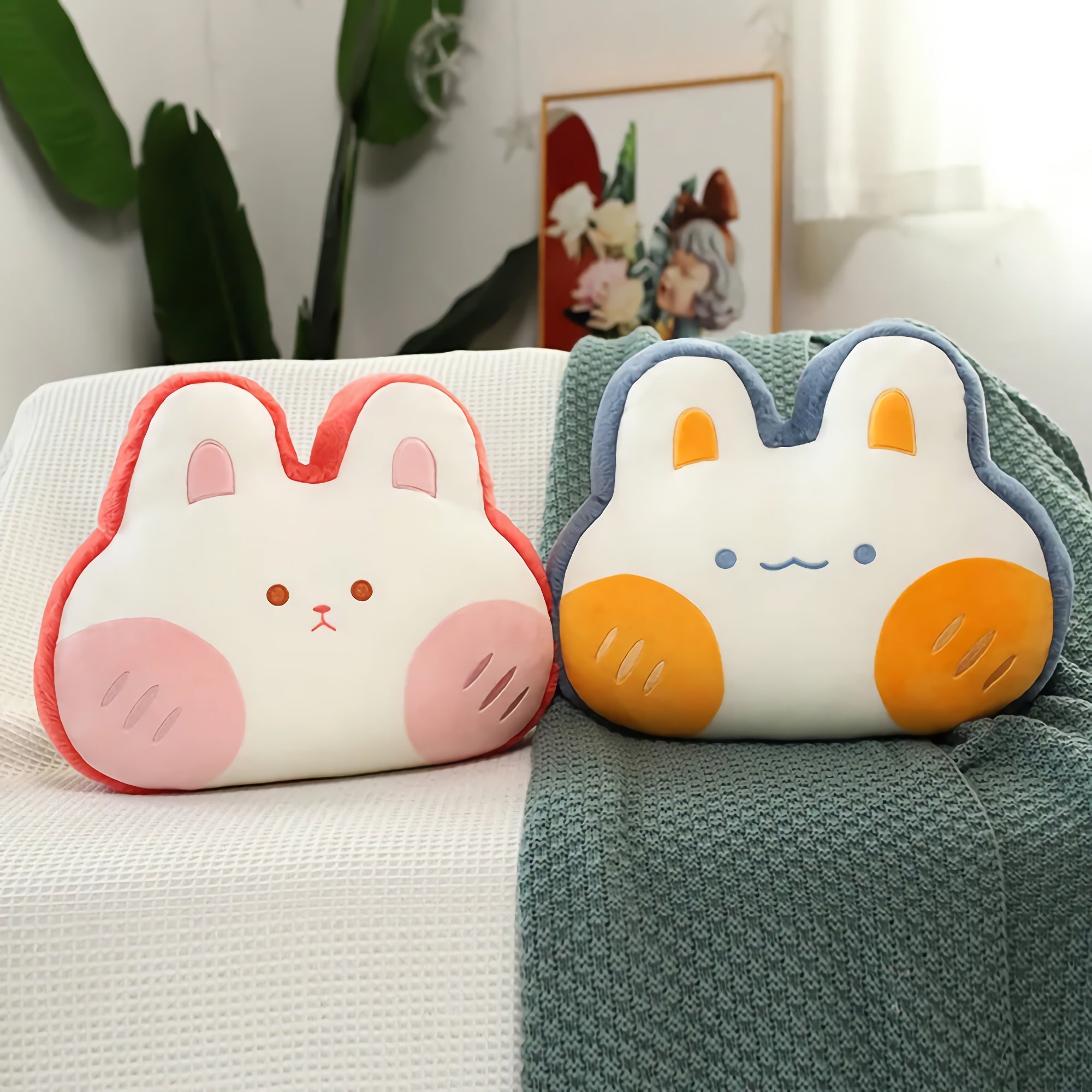 Two plush pillows shaped like bunnies with pink and orange accents on a textured blanket.