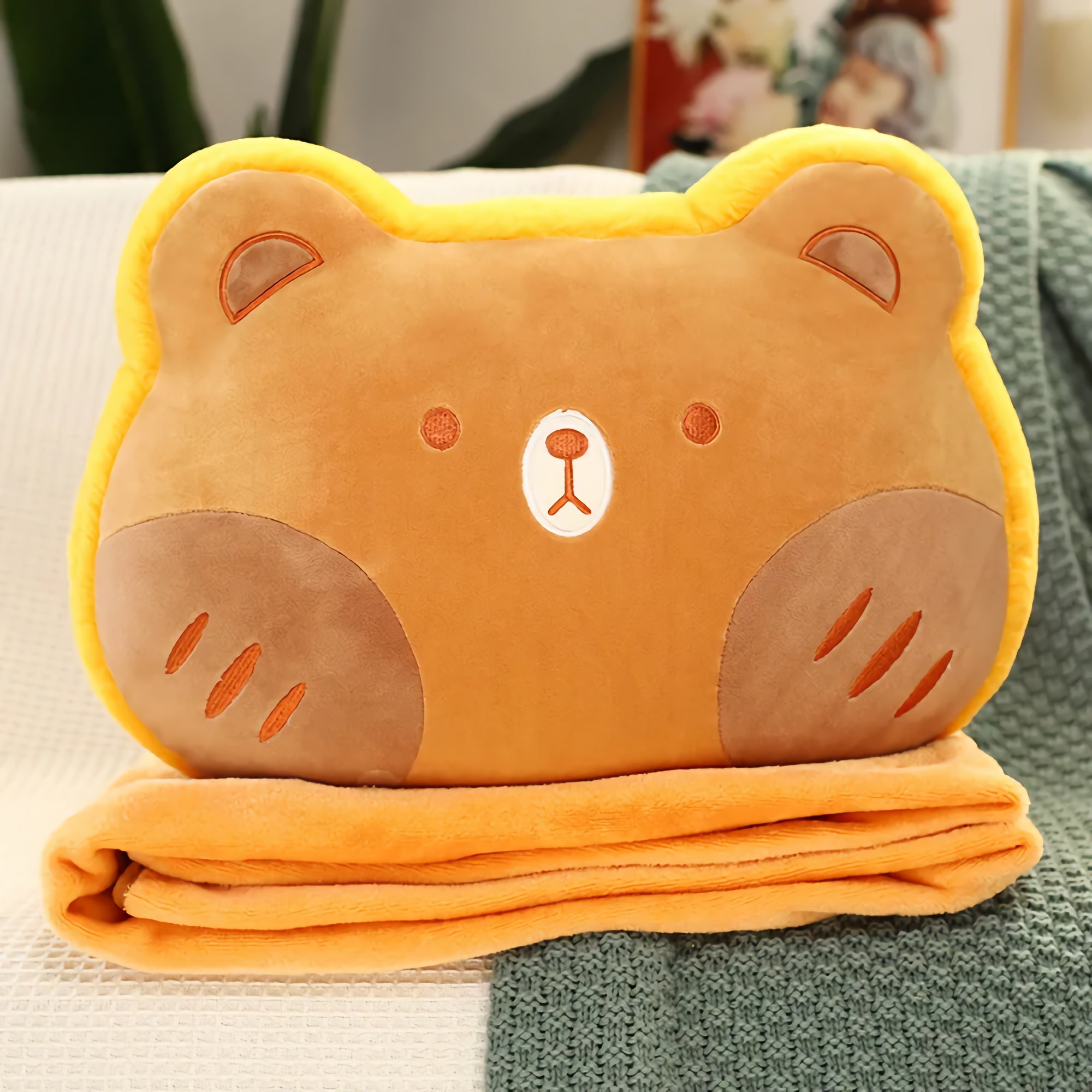 Plush bear-shaped pillow on top of a folded orange blanket.