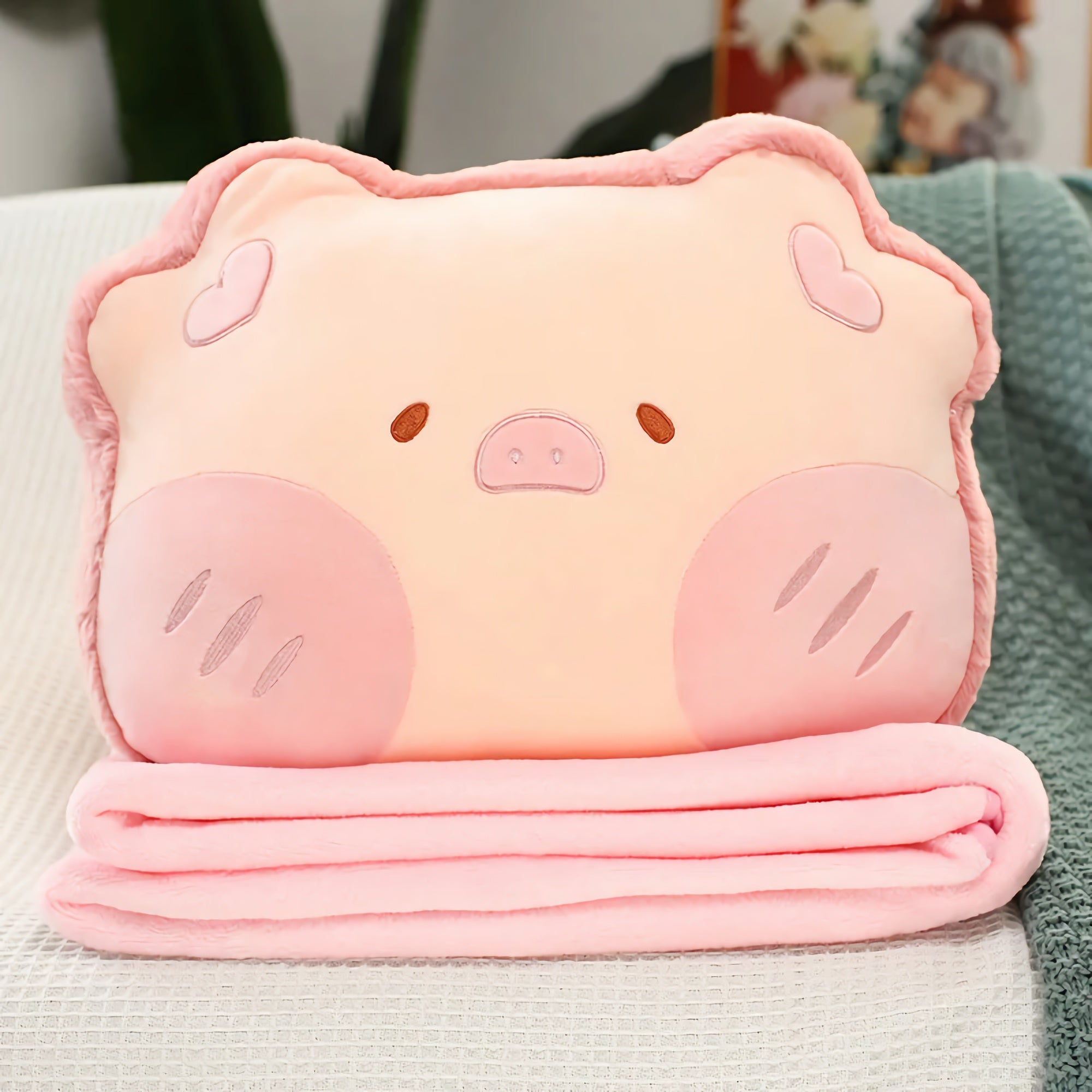 Plush pillow shaped like a pig with a pink blanket folded underneath it.