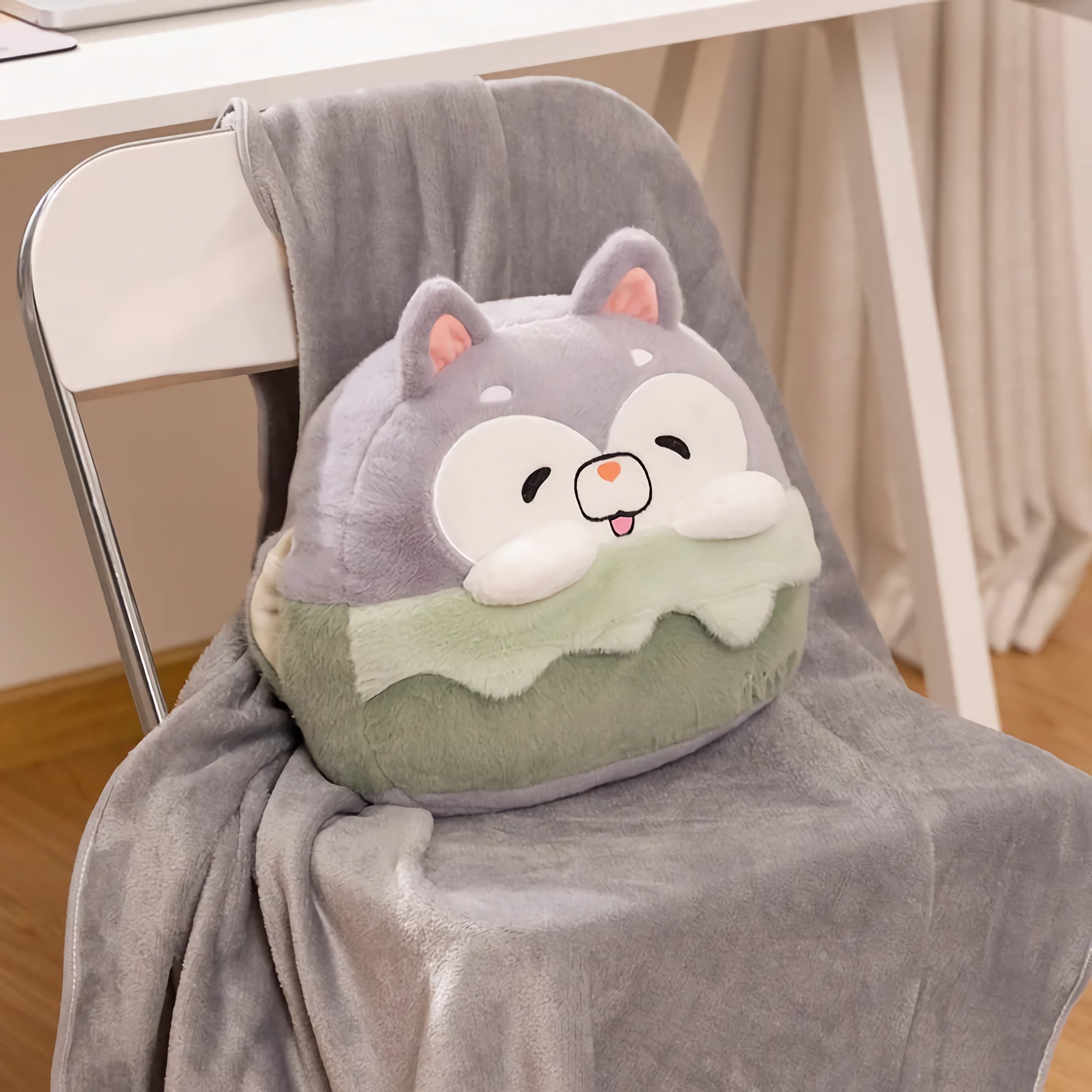 A plush pillow shaped like a cartoon animal rests on a gray blanket draped over a chair.