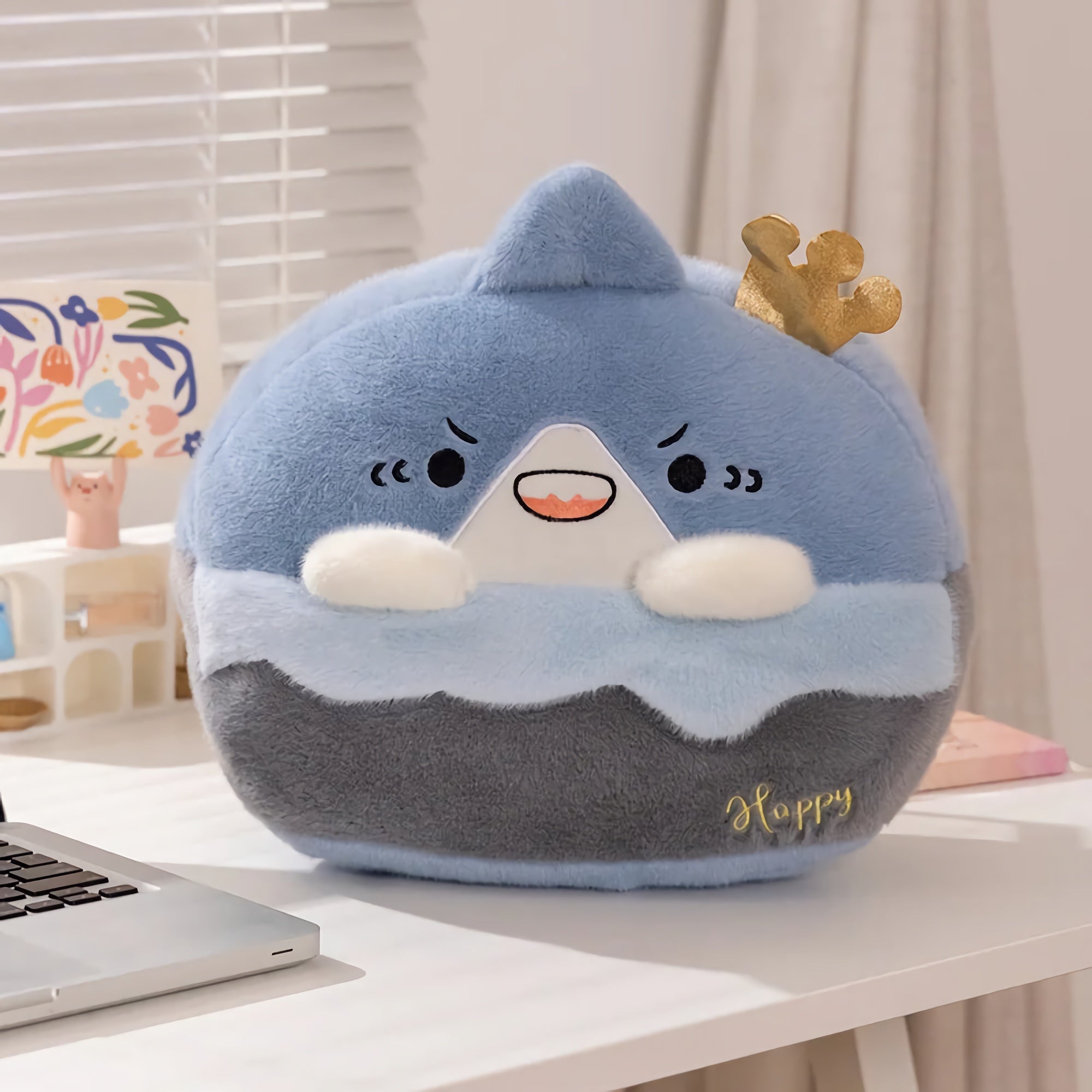 Plush pillow shaped like a blue mountain with a crown, featuring a smiling face and small arms.