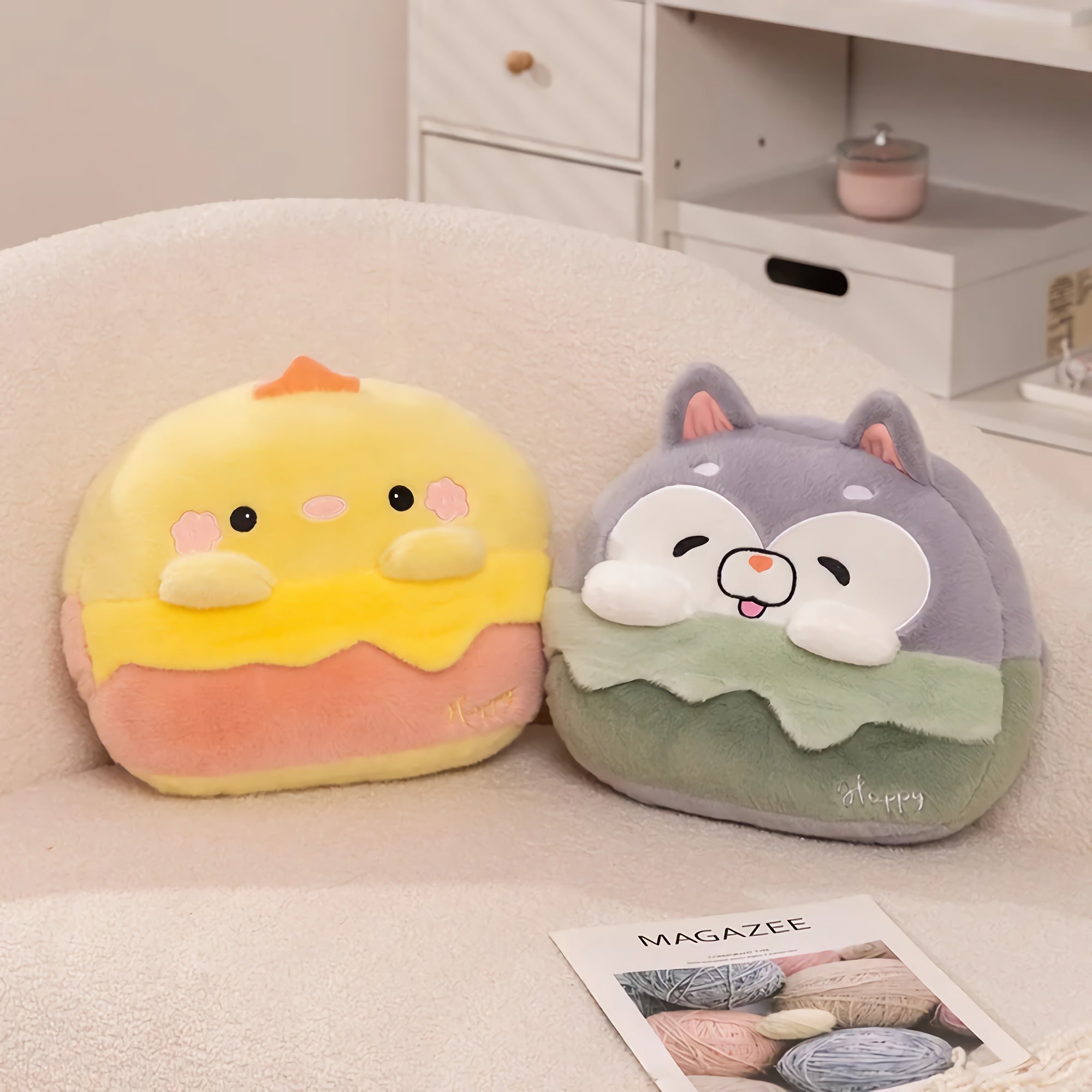 Two plush pillows shaped like a chick and a cat, sitting on a soft surface with a magazine nearby.