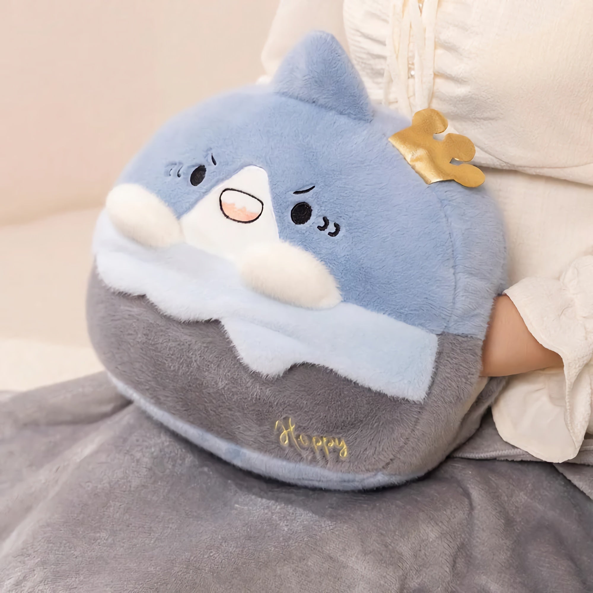Plush pillow shaped like a blue and gray animal with a crown, featuring a happy expression and soft fabric.