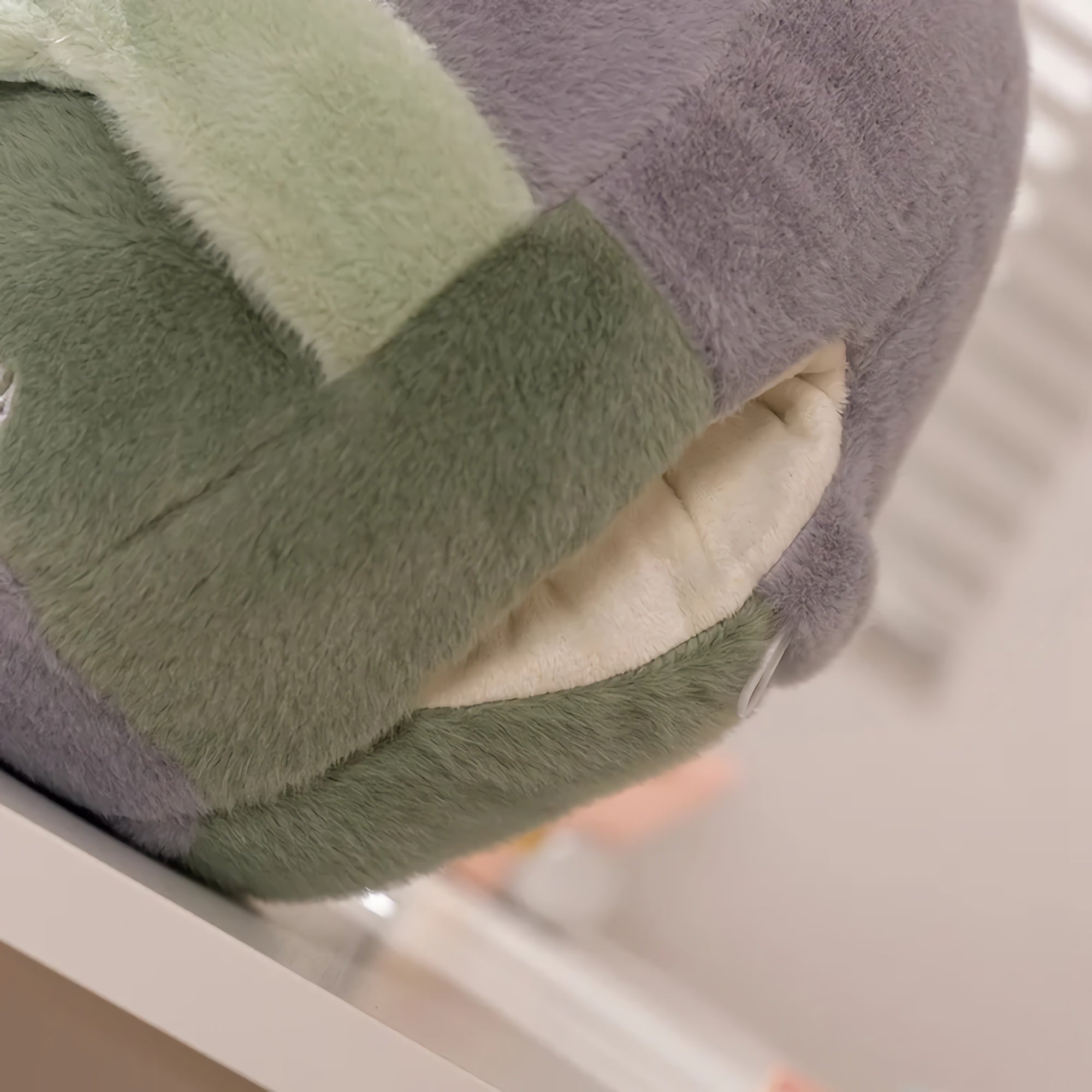 Plush pillow with a soft, textured surface in green and gray colors, resting on a white surface.