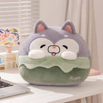 Plush pillow shaped like a cute animal with a smiling face, sitting on a desk beside a laptop and decorative items.