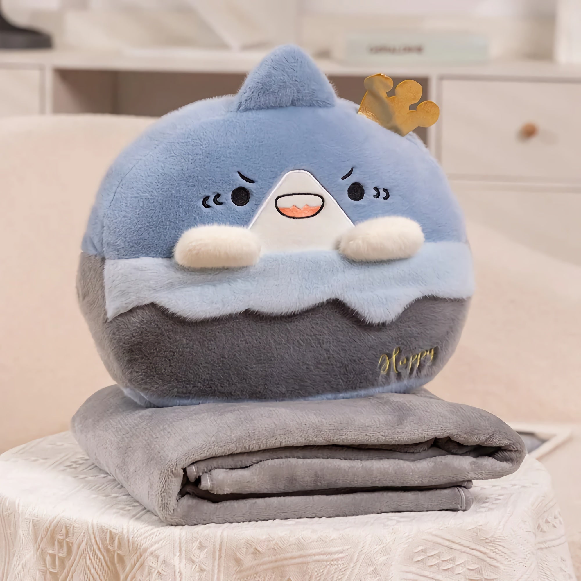 A plush pillow shaped like a blue mountain with a crown, resting on a folded gray blanket.
