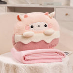 A plush pillow shaped like a dessert sits on a folded pink blanket on a table.