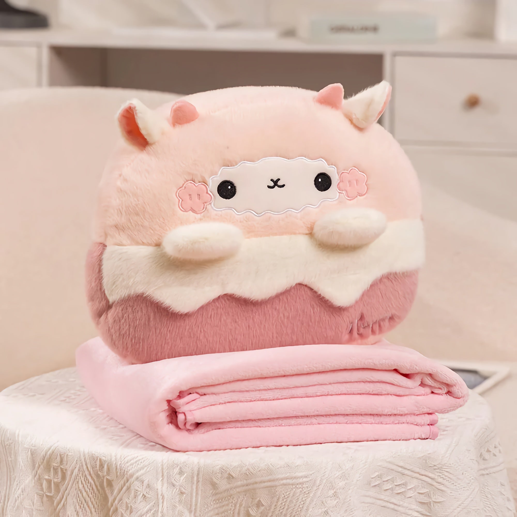A plush pillow shaped like a dessert sits on a folded pink blanket on a table.