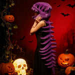 A person wearing a purple dinosaur skeleton plush hood and spine stands beside Halloween decorations.
