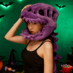 A person wearing a purple dinosaur skeleton plush hood and spine in a dimly lit room with Halloween decorations.