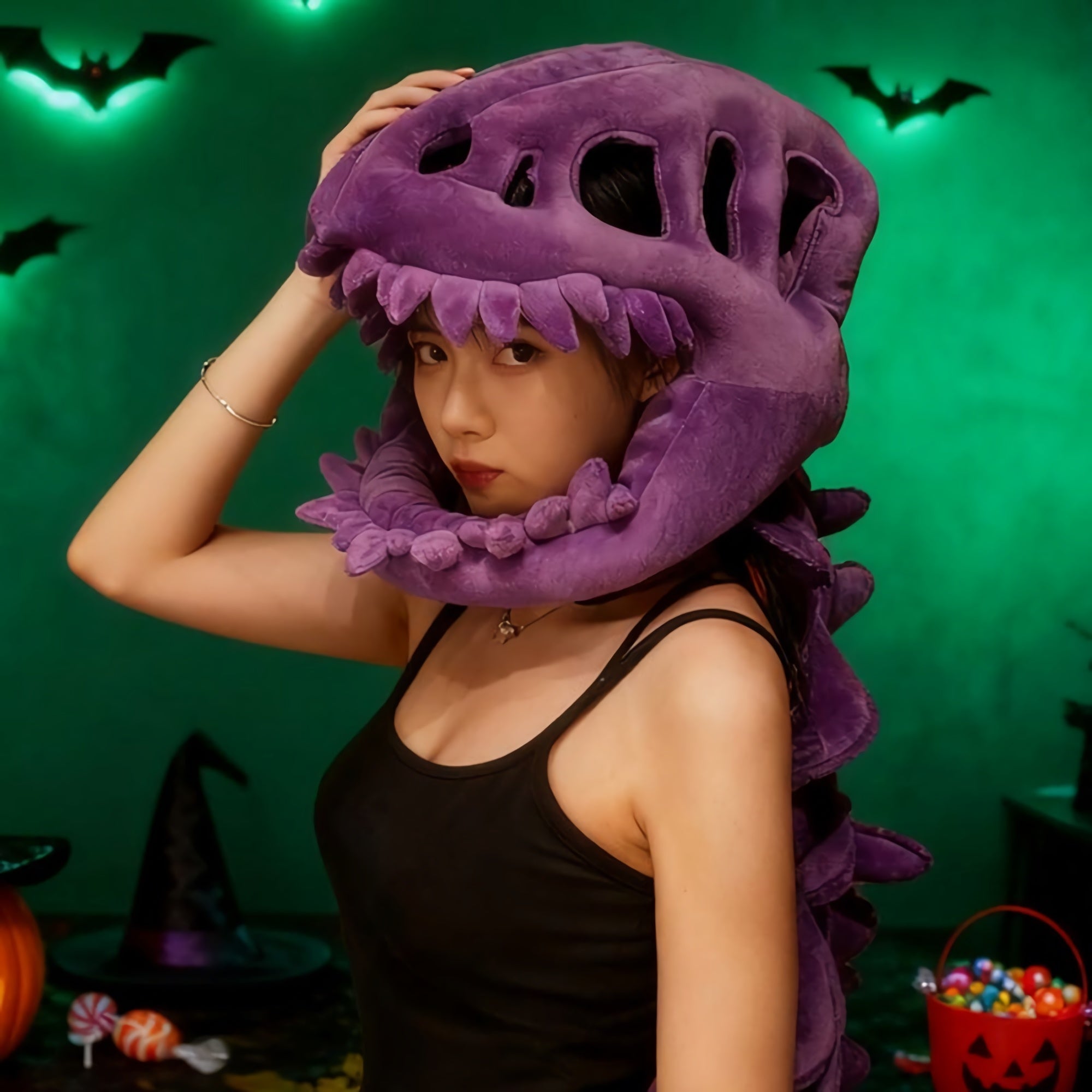 A person wearing a purple dinosaur skeleton plush hood and spine in a dimly lit room with Halloween decorations.