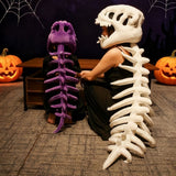 Two people sit with dinosaur skeleton plush hoods and spines, one in purple and the other in white, near Halloween decoration