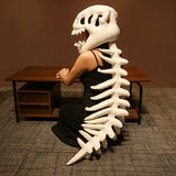 A person wearing a dinosaur skeleton plush hood and spine sits at a desk, facing away from the camera.