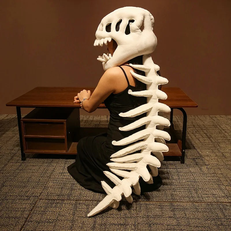 A person wearing a dinosaur skeleton plush hood and spine sits at a desk, facing away from the camera.