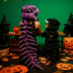 A person and a child wear dinosaur skeleton plush hoods and spines, sitting at a table with Halloween decorations.