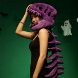 A person wearing a purple dinosaur skeleton plush hood and spine, posing against a green background.