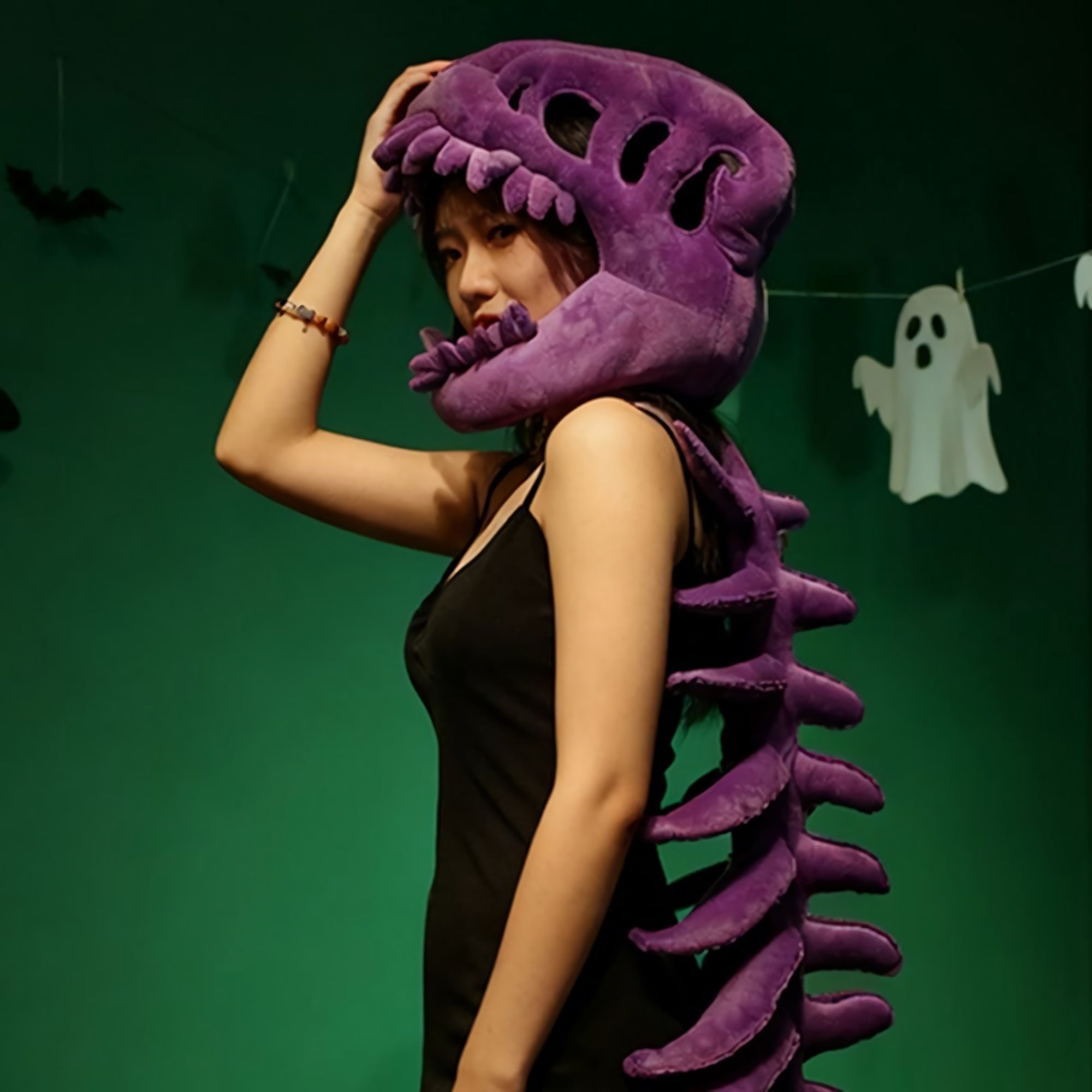 A person wearing a purple dinosaur skeleton plush hood and spine, posing against a green background.
