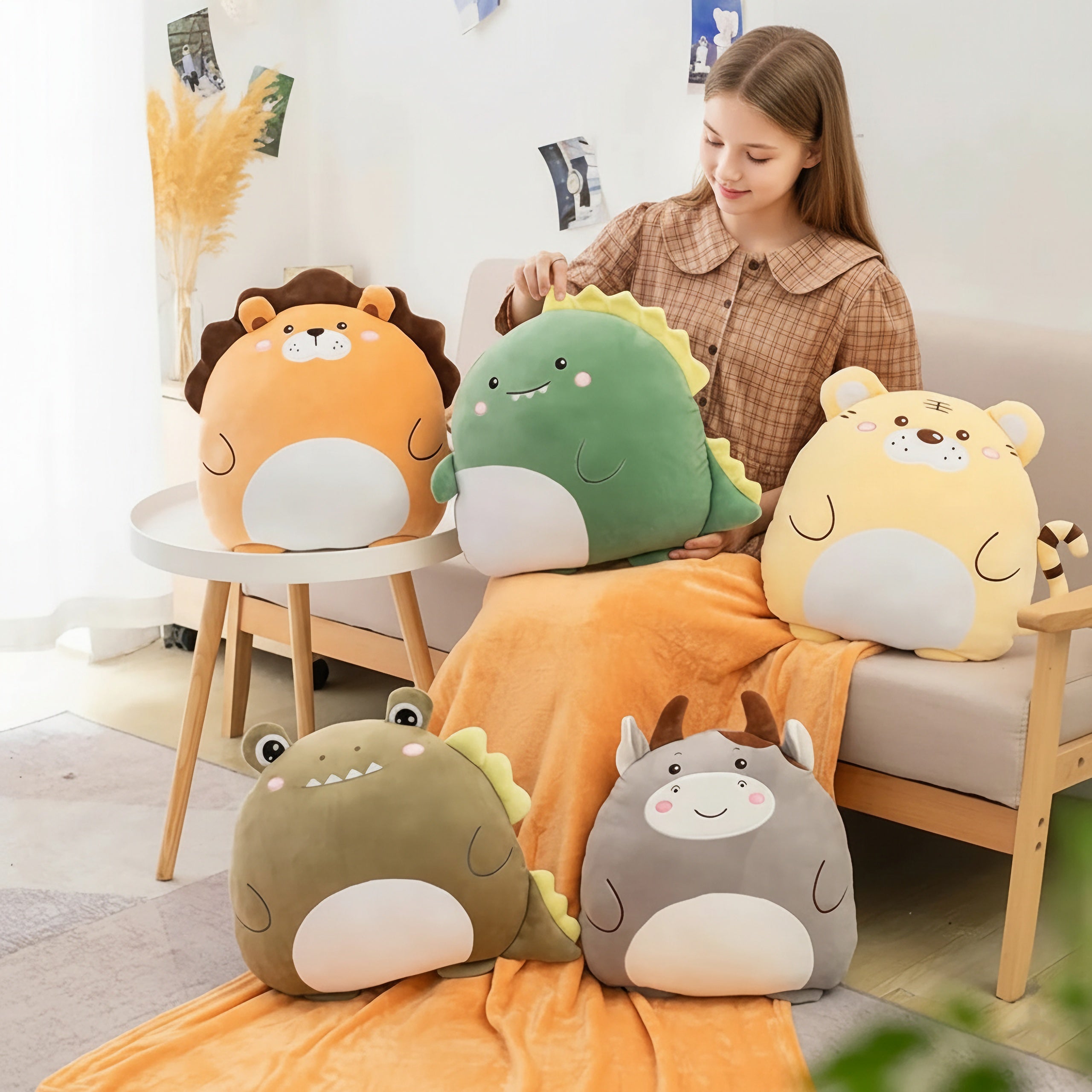 A girl sits on a couch with a travel blanket, surrounded by plush animal pillows in various colors and designs.