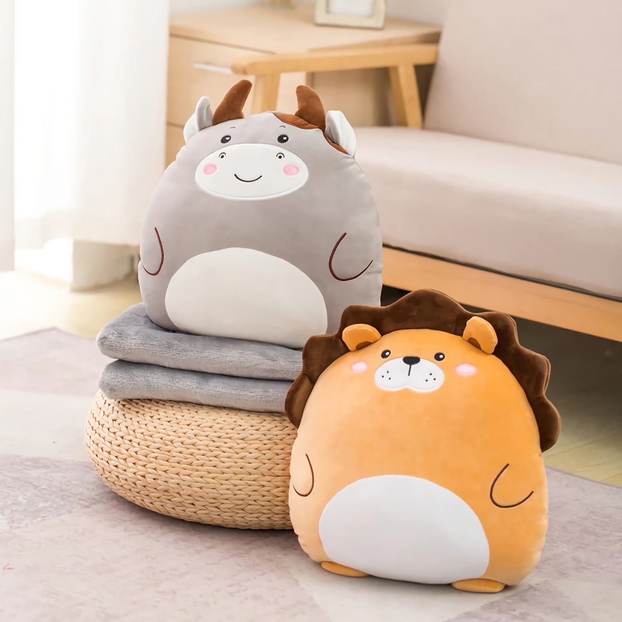 Two plush animal pillows, a gray cow and an orange lion, on a stack of folded blankets.