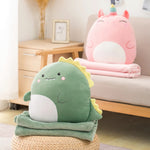 Green dinosaur plush pillow on a green blanket, with a pink unicorn pillow and blanket on a couch.