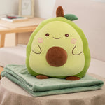 A plush avocado pillow sits on a folded green blanket on a table in a cozy setting.