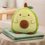 A plush avocado pillow sits on a folded green blanket on a table in a cozy setting.